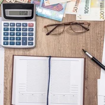 Calculator, eyeglasses, banknotes, and notebook on a desk